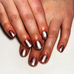 Short rounded nails in rose-gold metallic foil polish with reflective coppery shimmer finish.