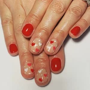 Short nails in nude and glossy red accented with small red and white hearts.