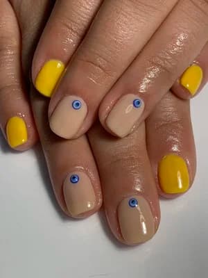 Short nails mixing yellow and nude bases with tiny blue evil-eye dot accents.