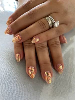Almond nails in warm orange and yellow with gold foil flake marble accents.