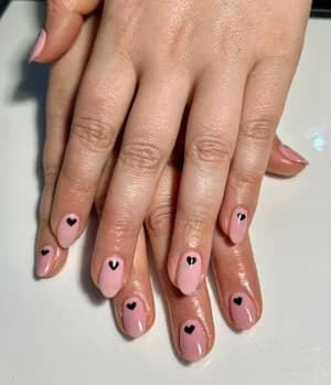 Short sheer pink nails each stamped with a small black heart accent.