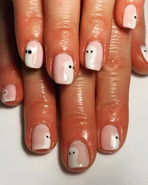 Short milky-pink and white nails painted with small ghost shapes and black dot eyes.