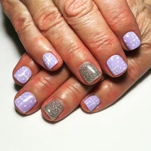 Short pastel lilac nails with white dots and snowflakes plus one silver glitter accent.