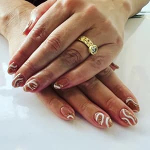 Reddish-brown nails with white swirling wave line patterns, gold ring on finger.