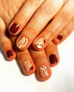 Short nails mixing solid maroon and nude with abstract white and rust wave swirls.