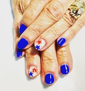 Short cobalt blue nails with a nude accent nail featuring red, white, and blue stars.