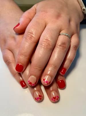 Short glossy red nails with negative-space tips accented by small red and pink hearts.