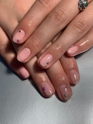 Glossy sheer pink nails accented with tiny colorful rhinestone gems near the cuticles.