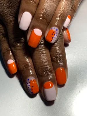 Orange and pale pink color-block nails with purple and black polka-dot cluster accents.