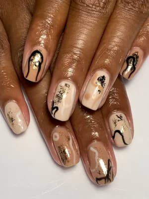 Nude beige nails with abstract black line art and scattered gold foil flake accents.