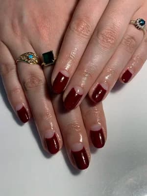 Short square nails in glossy solid dark burgundy red, worn with gold rings.