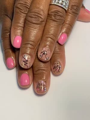 Pink and nude nails with black abstract script lettering and gold dot accents.