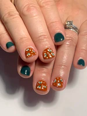 Dark teal solid nails paired with burnt orange nails and white floral dots.