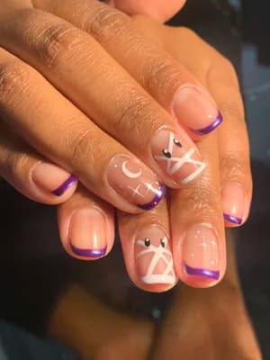 Nude nails with purple French tips and white line art, crosses, and moon accents.