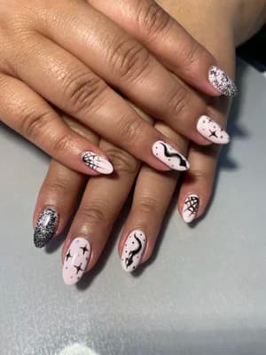 Pale pink almond nails with black spiderweb, stars, squiggles, and silver glitter accents.