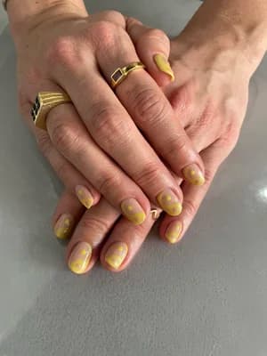 Pale yellow short nails with white daisy florals and thin gold swirl accents.