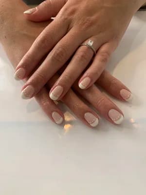 Short natural nails with a classic white-tipped French manicure over a glossy nude base.