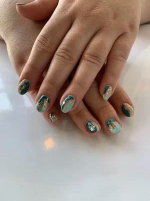 Short nails in teal and emerald green marble swirls accented with gold foil flakes.