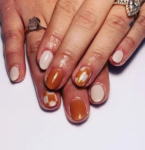 Short glossy nails in caramel brown and cream nude with abstract white splotch accents