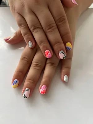 Mismatched short nails mixing silver glitter, pink leopard print, florals and cow-spot patterns