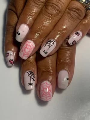 White and nude nails with pink and black spiderwebs, tiny ghost, bat, and heart accents