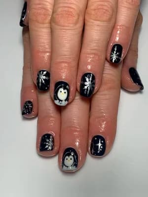 Dark navy nails painted with white snowflakes and hand-drawn penguins, winter theme