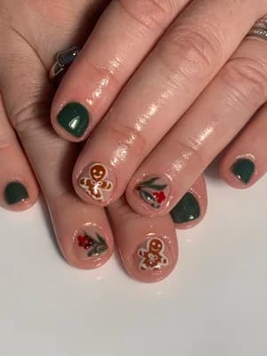 Nude and dark green nails featuring gingerbread men, holly berries, and a Christmas bell
