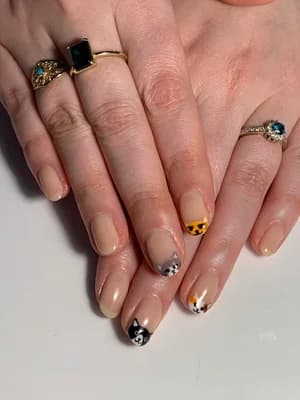 Neutral nails with leopard, cow-spot, and orange animal-print French tips, jeweled rings visible