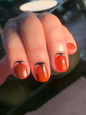 Short burnt-orange nails with black dripping paint design near the cuticle.