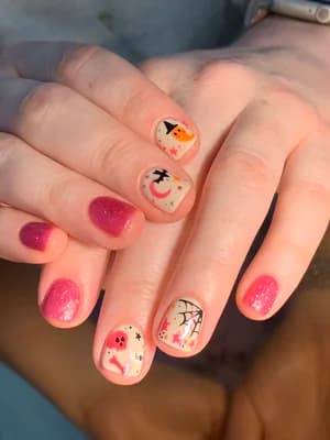 Short nails mixing pink glitter with cream Halloween art: ghosts, moon, spiderweb, characters.