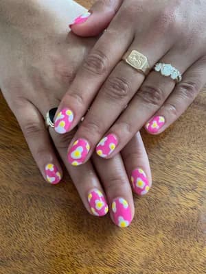 Round nails with hot pink, yellow, and white abstract cow-print blotch pattern.