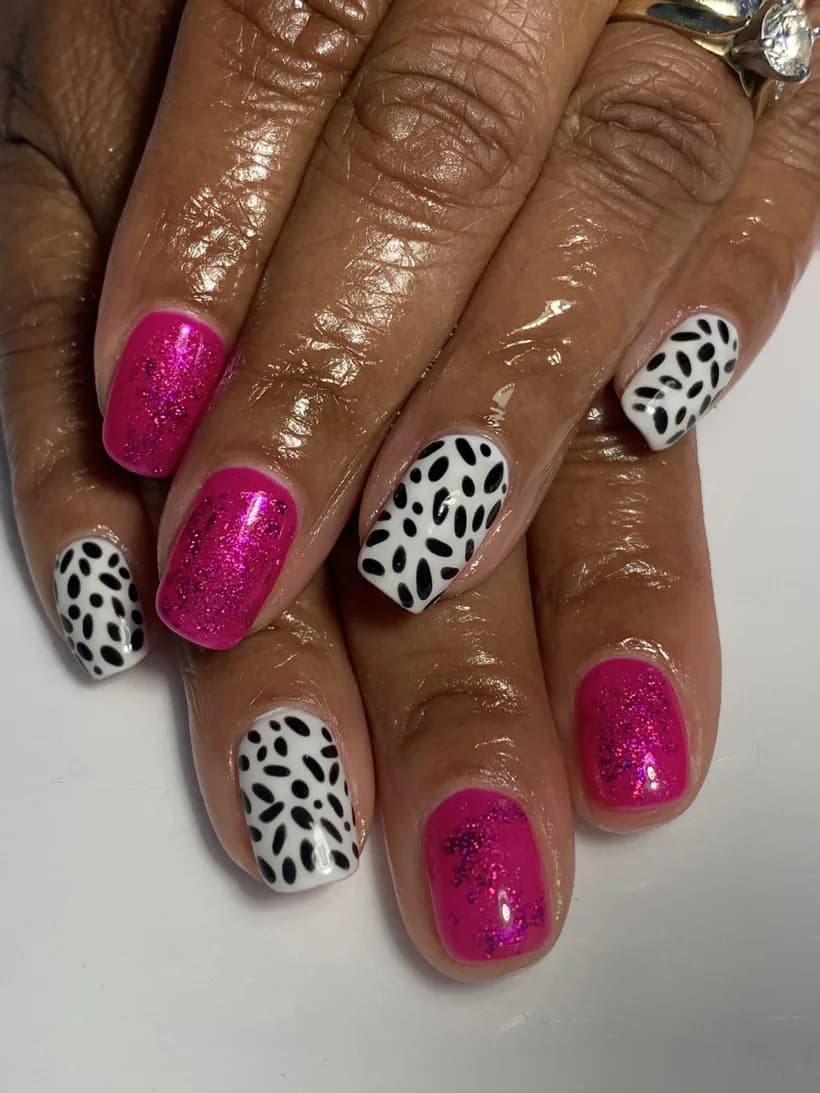 Short glossy nails alternating hot-pink glitter and black-and-white dalmatian-spot designs.