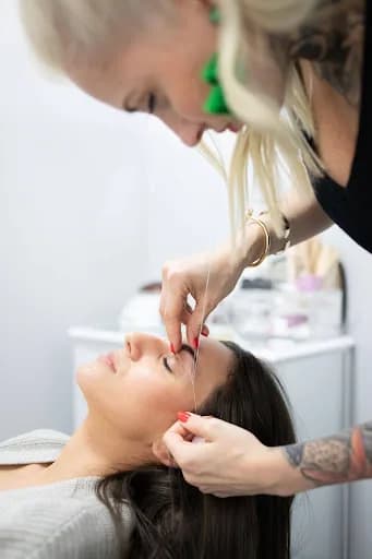 A technician threading a reclining client's eyebrow at Sacred Scarab Nail Boutique.